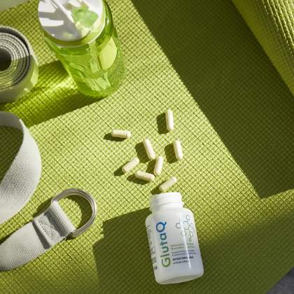 Opened bottle of GutaQ with veggie capsules spilled out on a yoga mat.